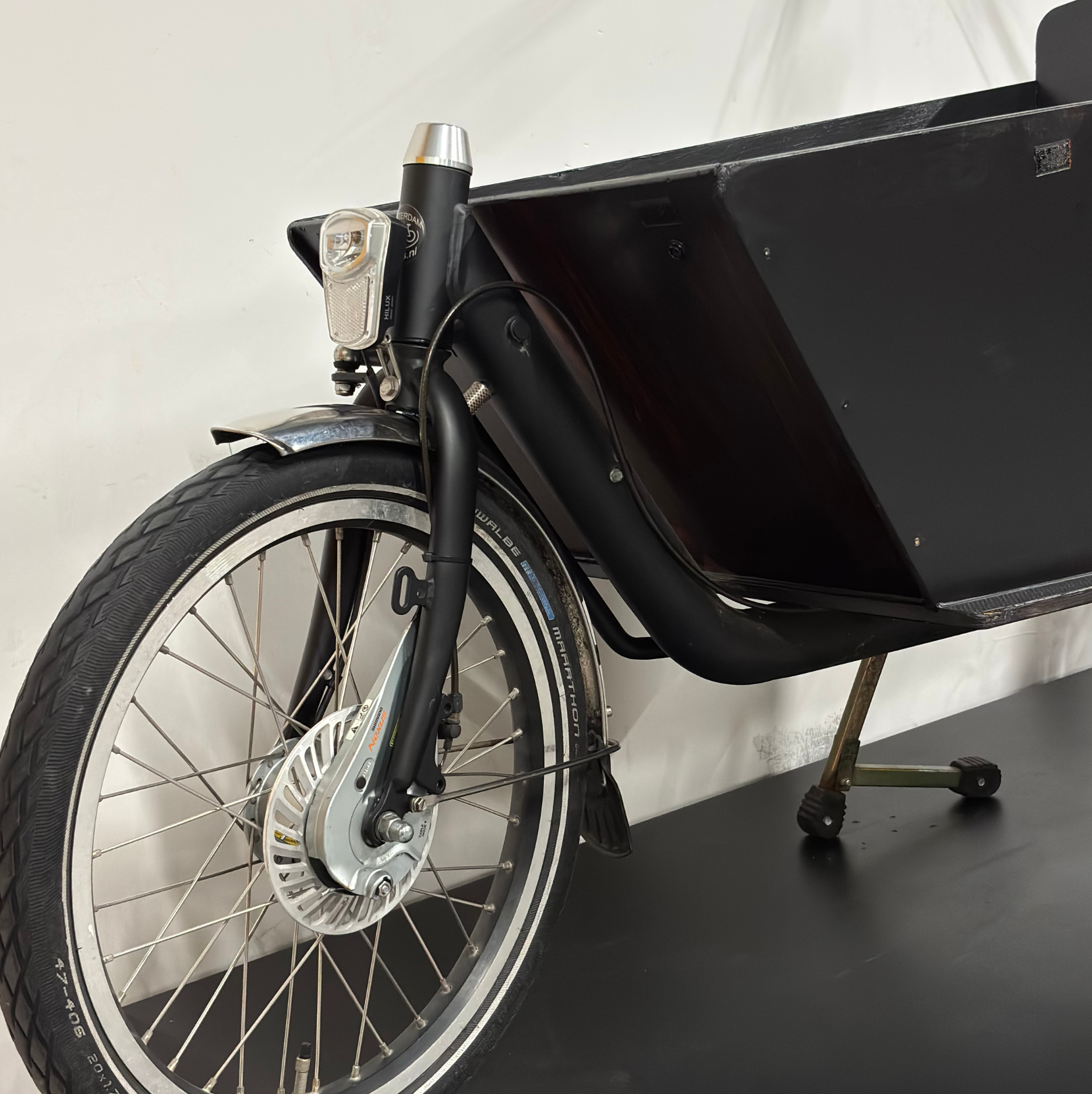 Gros plan sur la roue avant du vélo cargo électrique noir WAP Lille, avec phare, garde-boue, frein tambour et caisse avant