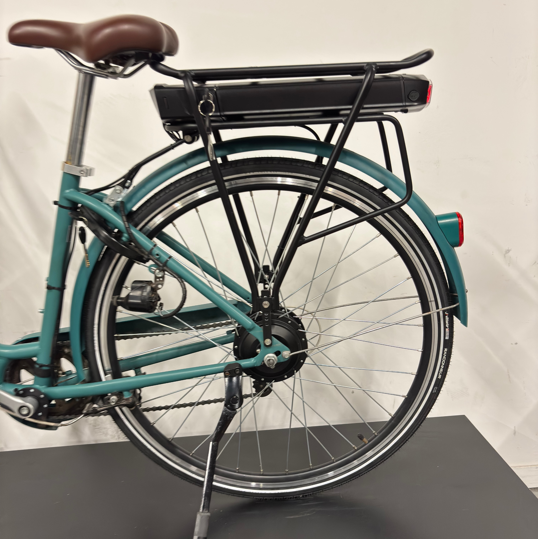 Vue arrière du vélo de ville électrique vert WAP Lille, cadrage sur la selle marron, la roue arrière, la batterie sur porte-bagages et le moteur de roue