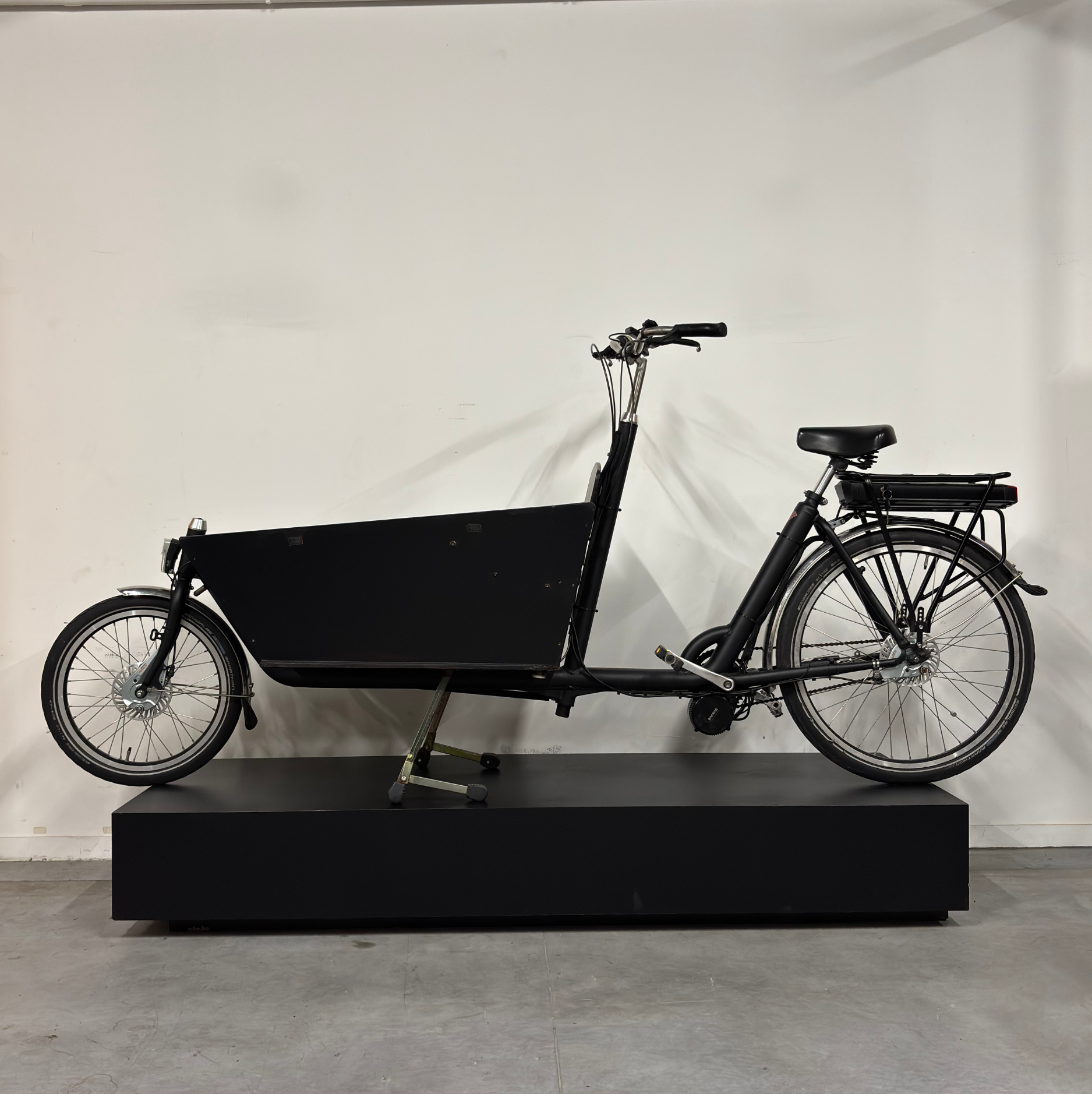 Vélo cargo électrique noir WAP Lille, vu de profil côté droit sur présentoir noir, avec grande caisse avant et batterie sur porte-bagages