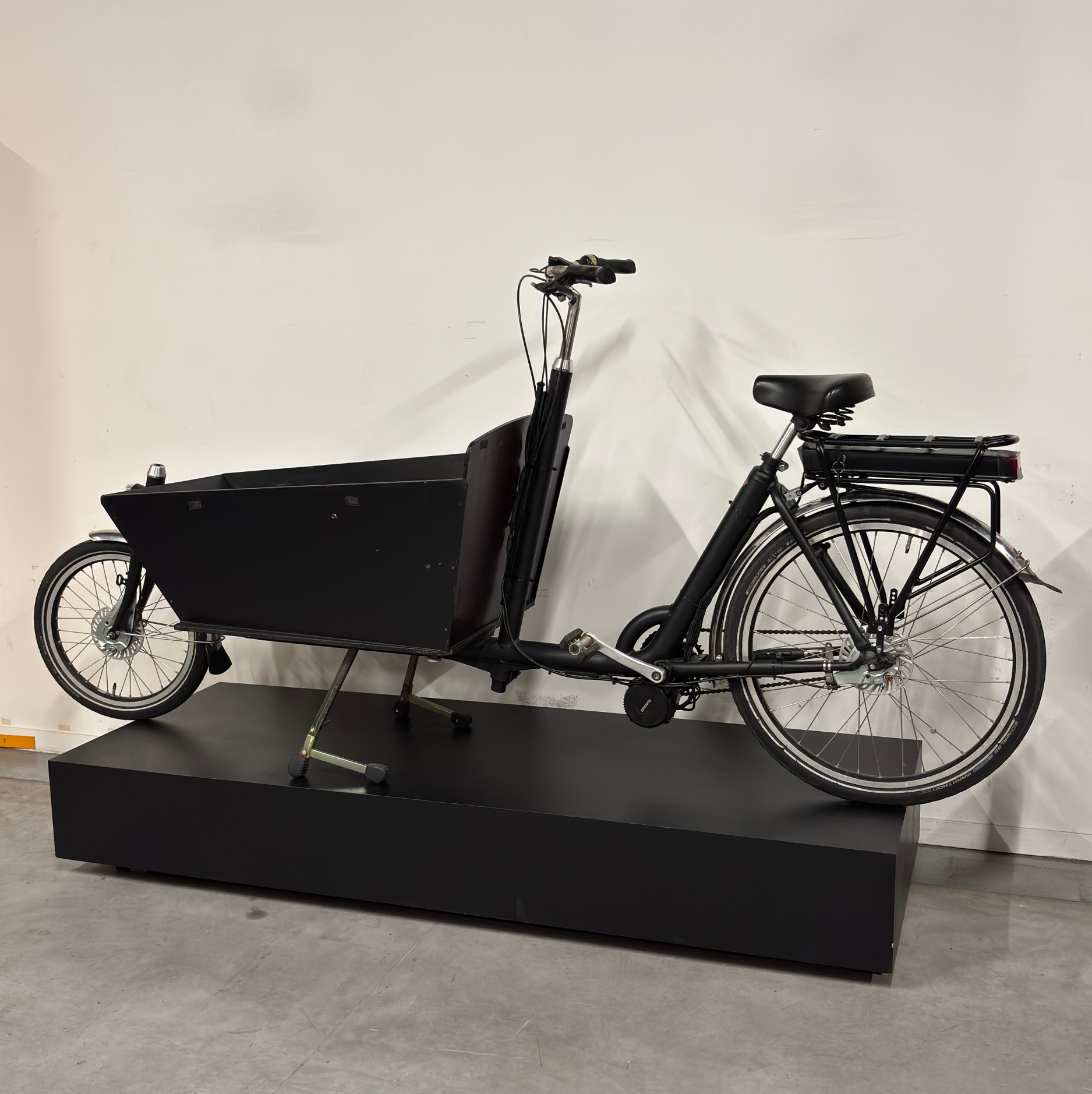 Vélo cargo électrique noir WAP Lille, vu de profil sur présentoir noir, avec grande caisse avant, roue avant de petit diamètre et batterie sur porte-bagages arrière